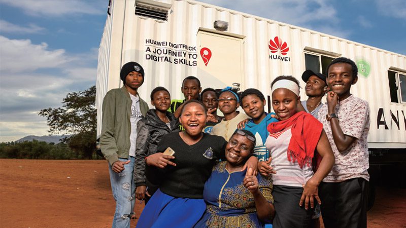 Kids posing and smiling in front of the DigiTruck with an older woman. 
