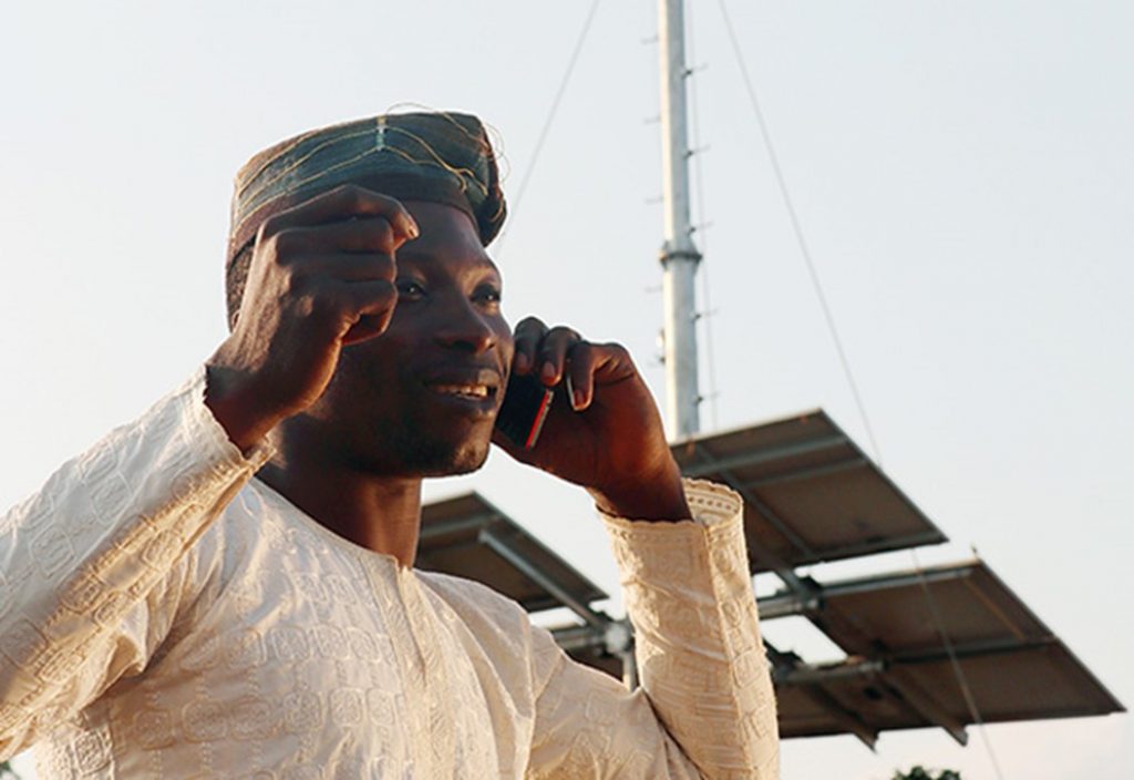 Man in Africa using cellphone in front of antenna.