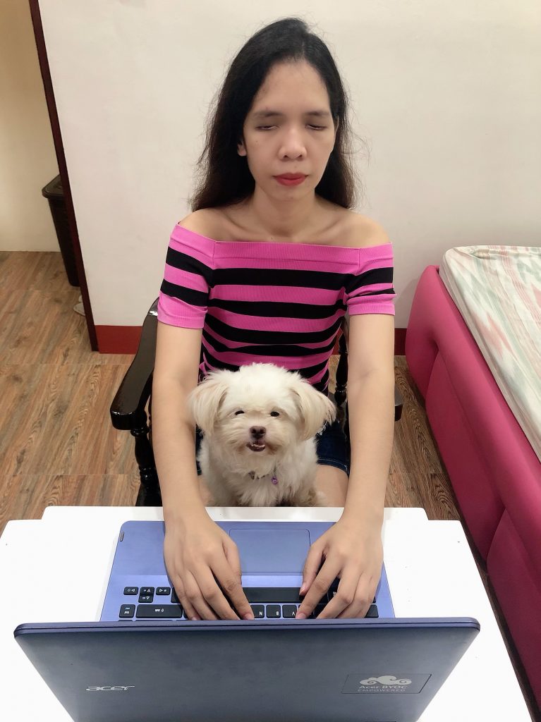 Jasmin Ambiong using a laptop with a dog in her lap.
