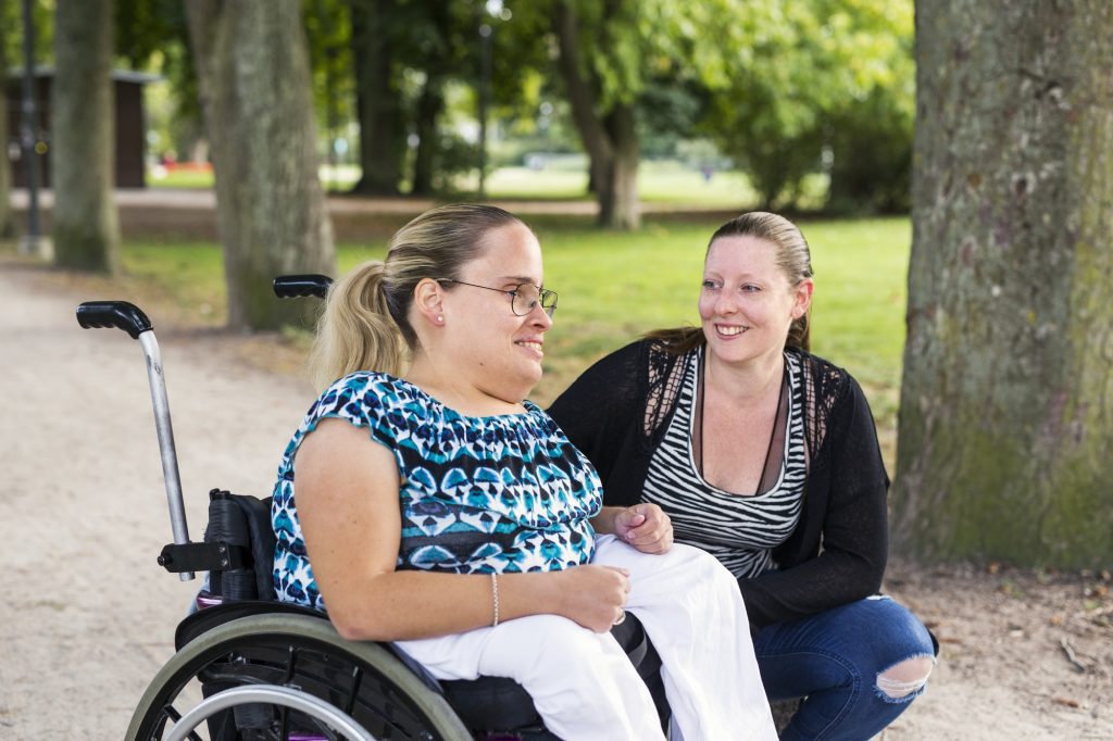 Disabled woman in wheelchair with assistant in park
